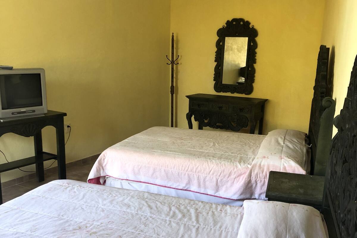 Una habitación con dos camas, una mesita con un televisor y un espejo en la pared.
