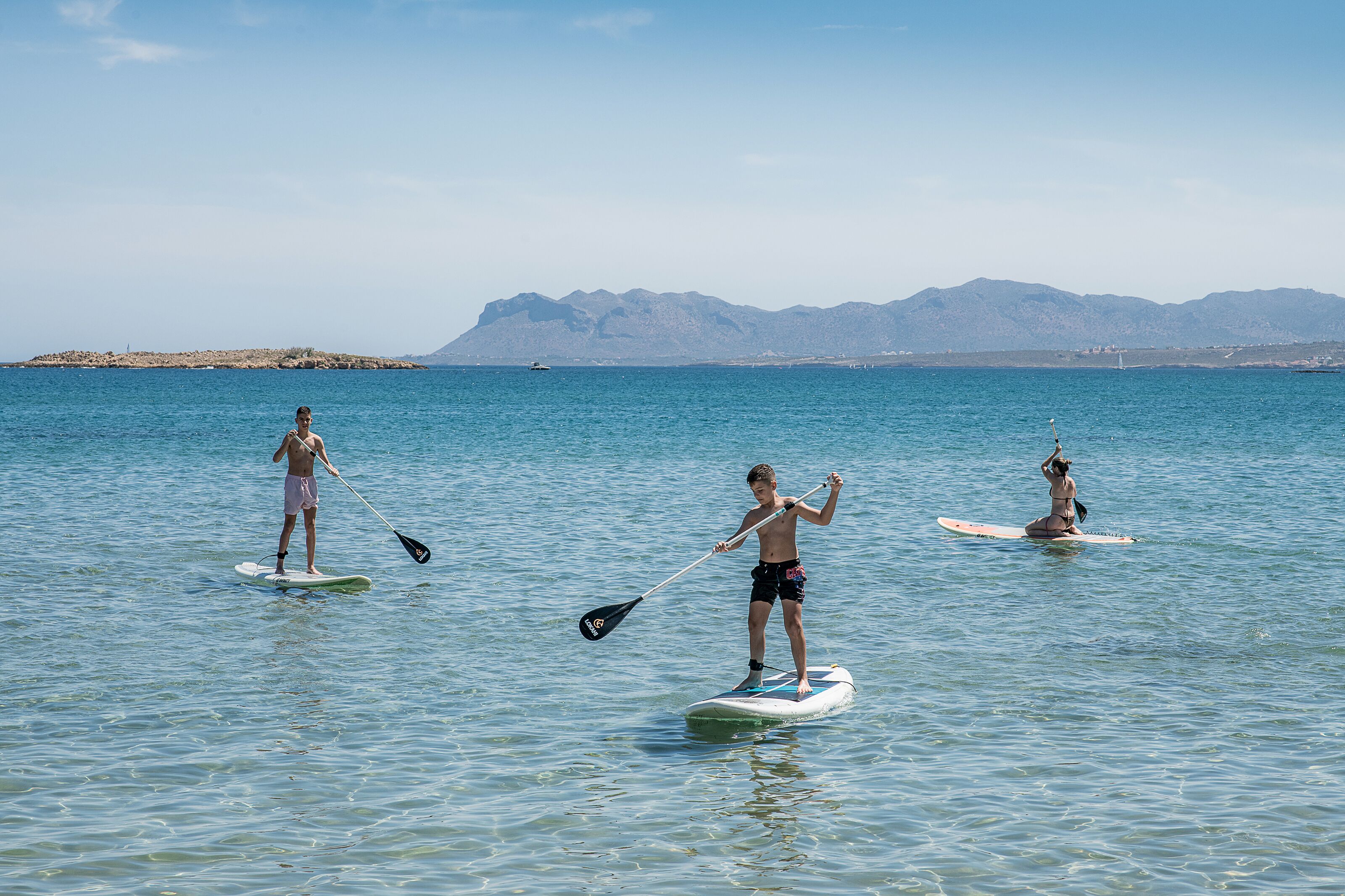 Three people paddleboarding on a calm sea with mountains in the background.