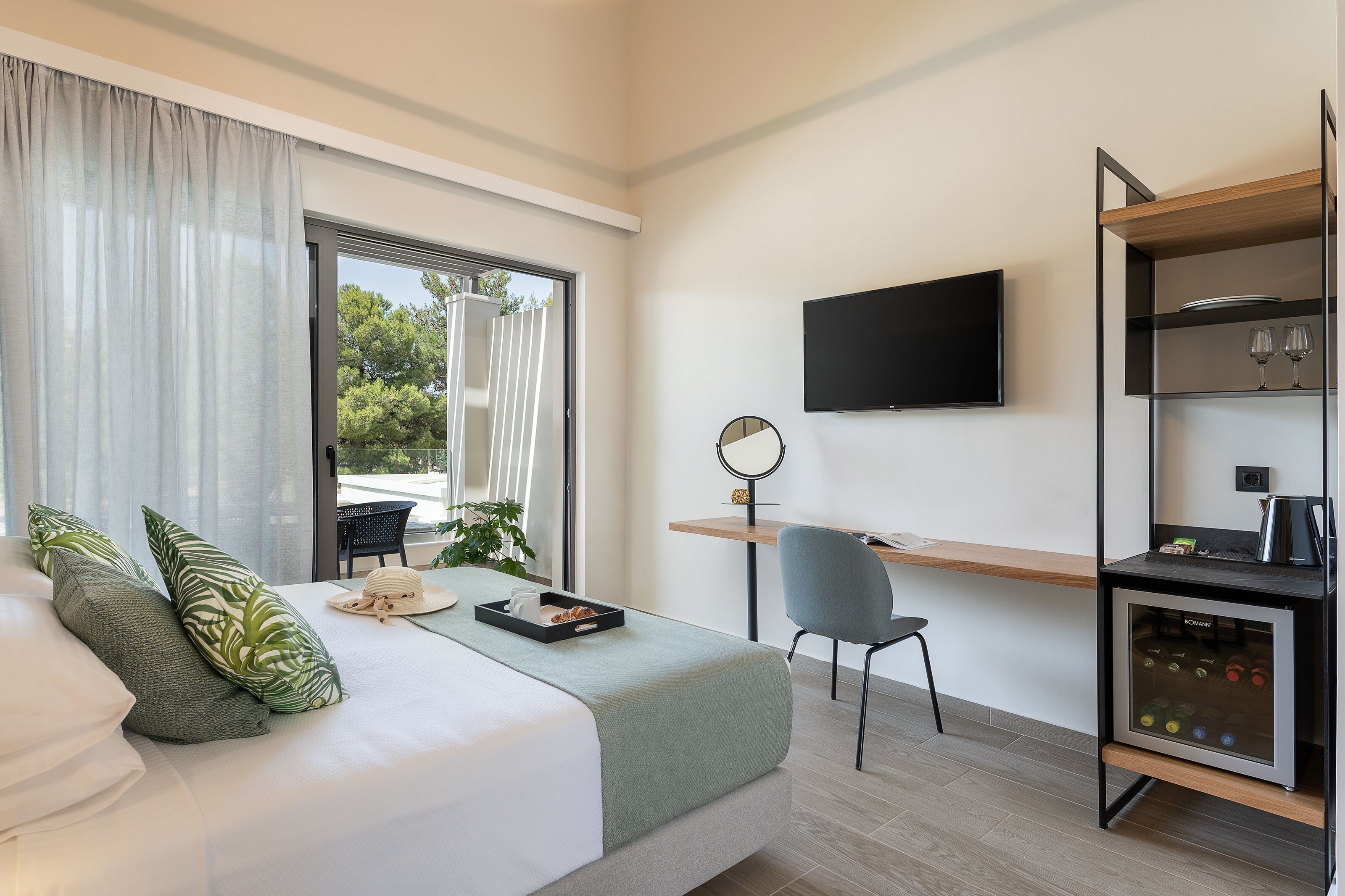 A modern hotel room with a bed, a desk, a chair, a TV, and a minibar.