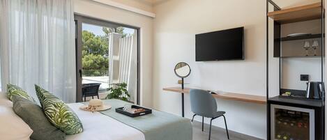 A modern hotel room with a bed, a desk, a chair, a TV, and a minibar.