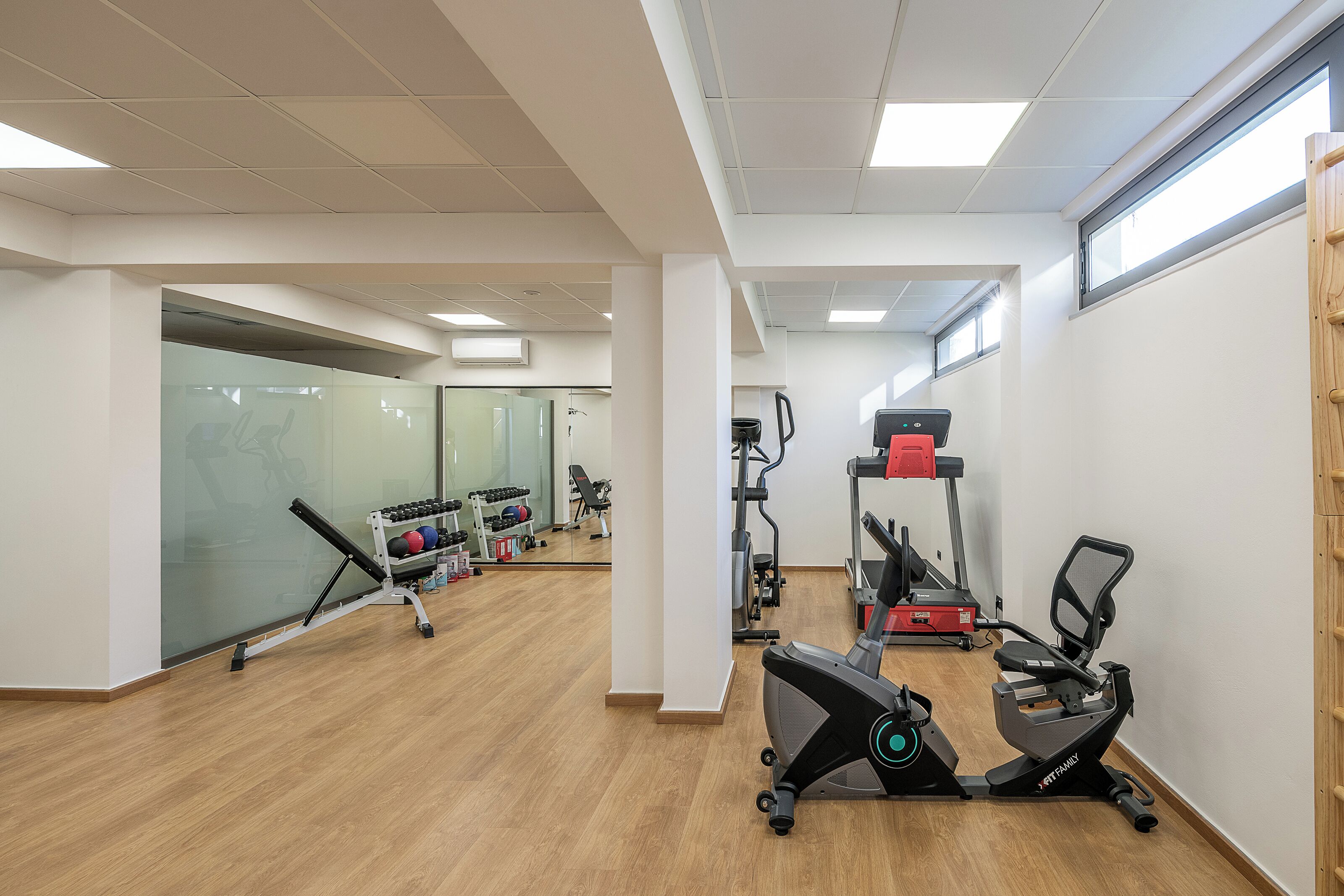 Ein Fitnessstudio mit Laufbändern, Krafttrainingsgeräten und einer Spiegelwand.