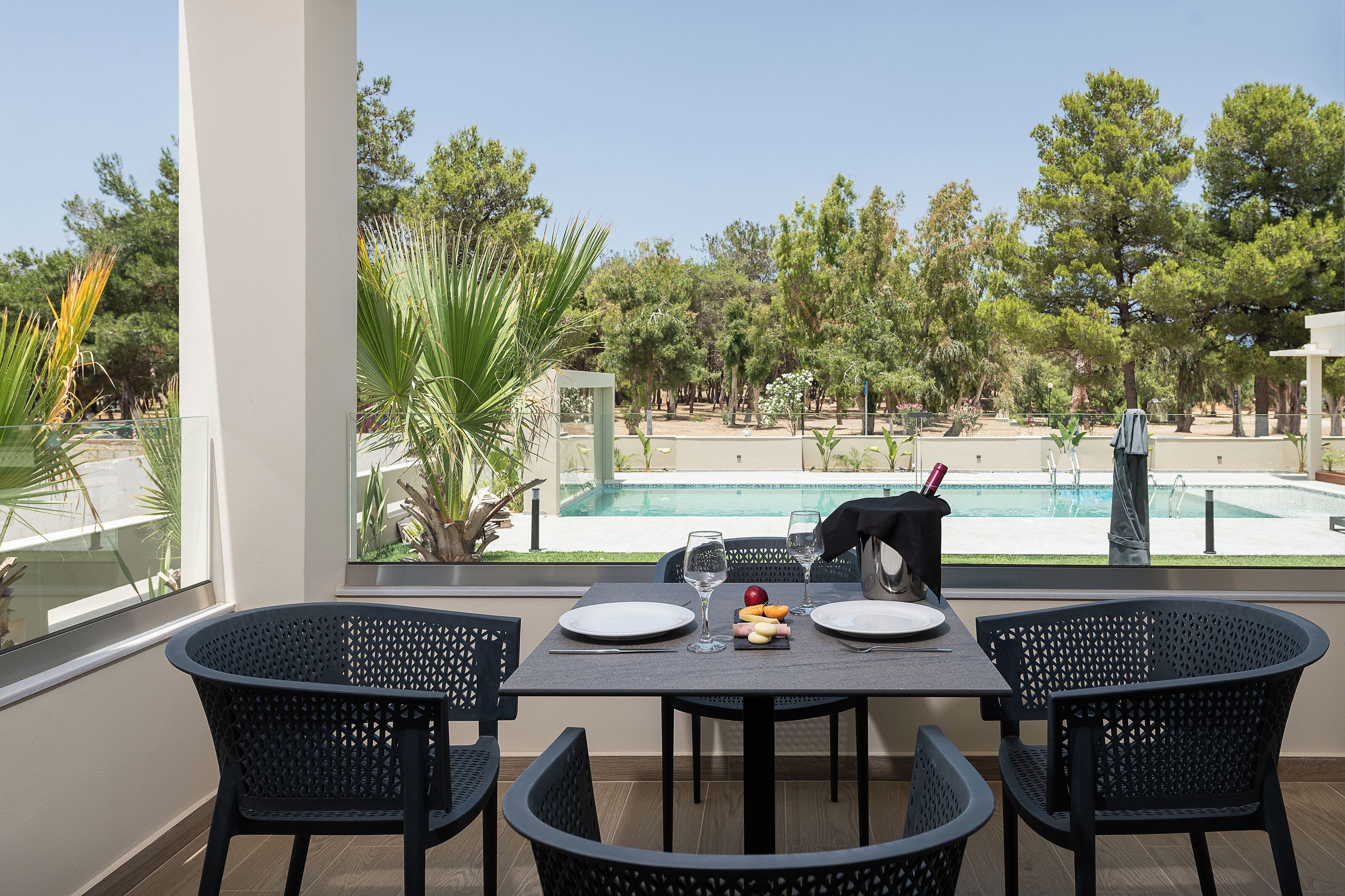 Een eethoek met een gedekte tafel voor twee, met uitzicht op een zwembad, omringd door bomen.