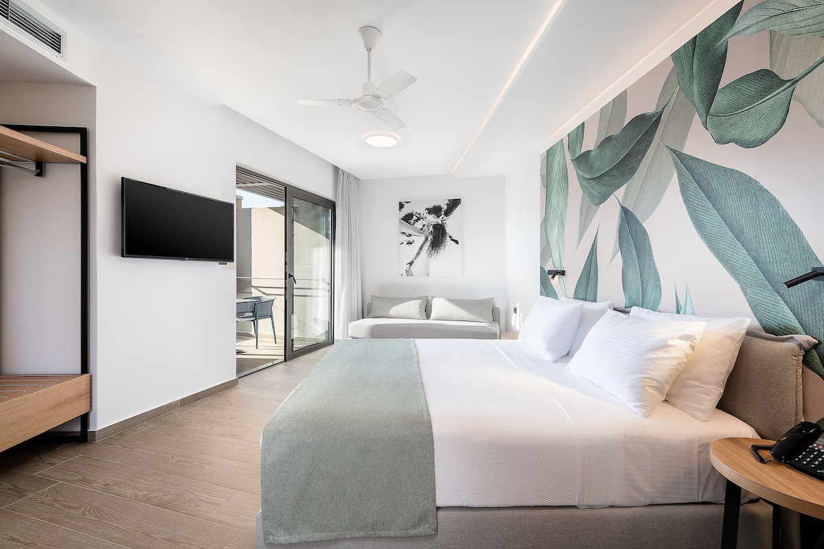 A modern hotel room with a bed, a desk, a flat-screen TV, and a large window.