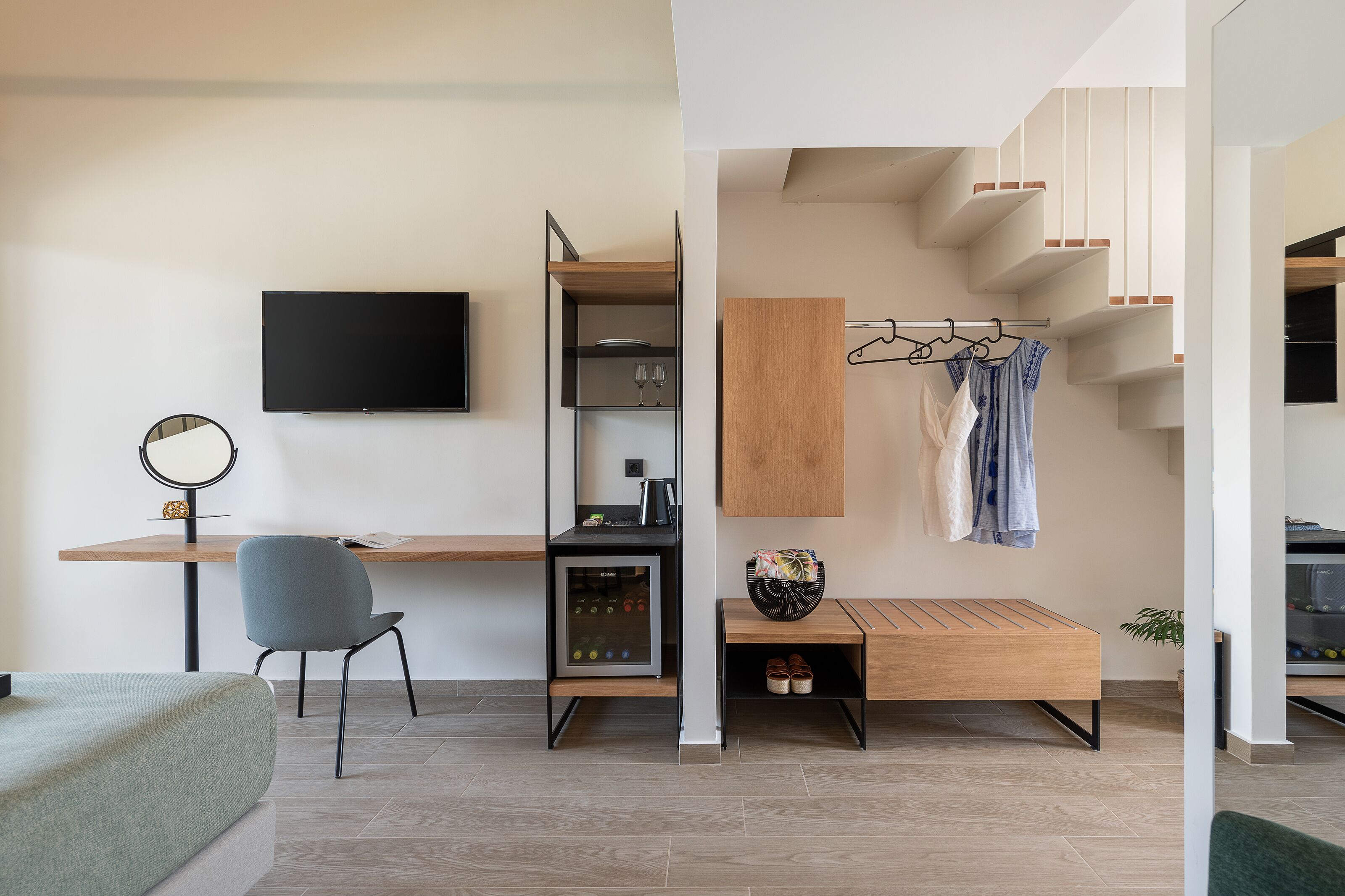 A modern, compact room with a bed, a desk, a chair, a TV, a mini-fridge, and a coat rack.