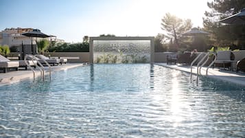 Una piscina al aire libre, sombrillas, sillones reclinables de piscina