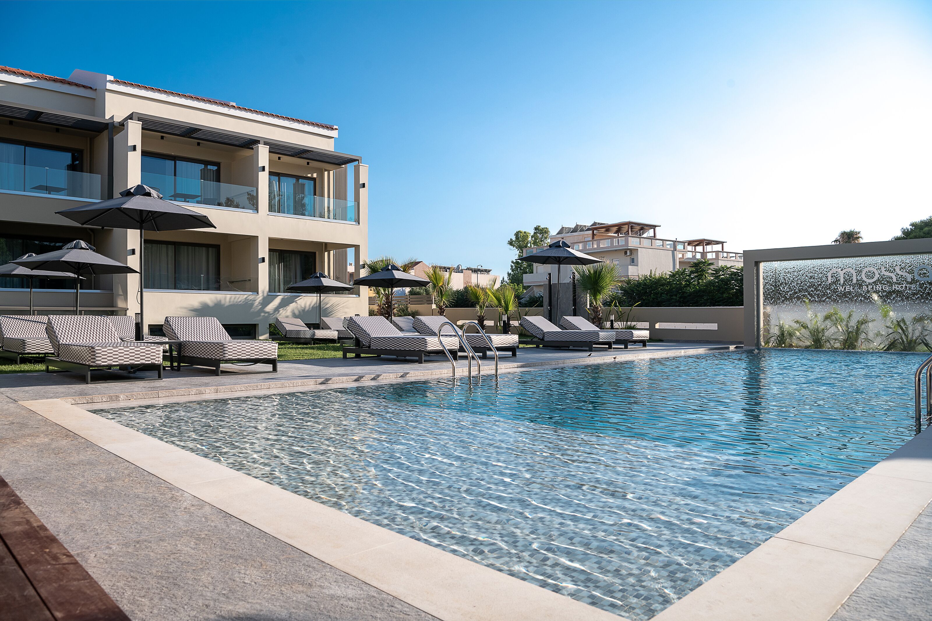 A modern hotel with a swimming pool, sun loungers, and umbrellas.