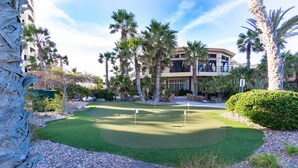 Un campo da golf ben curato con un putting green, circondato da palme e un edificio sullo sfondo.