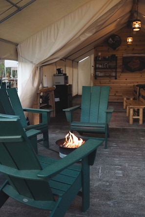 A tent with green chairs and a fire pit.