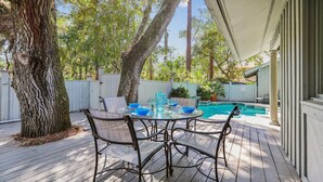 A wooden deck with a glass-top table and chairs, a swimming pool, and a white fence. - Beautiful Home w/ a Short Walk to the Beach! (Hilton Head Island)