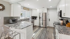 A modern kitchen with white cabinets, a stainless steel refrigerator, a built-in oven, and a granite countertop. - Beautiful Home w/ a Short Walk to the Beach! (Hilton Head Island)