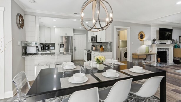A modern kitchen with white cabinetry, a central island, and a dining area with a black table and white chairs. - Beautiful Home w/ a Short Walk to the Beach! (Hilton Head Island)