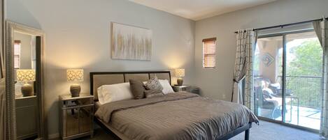 A bedroom with a large bed, bedside lamps, a mirror, and a view of the outdoors through a sliding glass door.