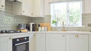 Eine Küche mit weißen Schränken, einem Herd, einer Kaffeemaschine und einem Fenster mit einer Pflanze.