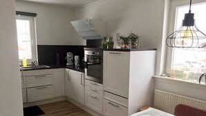 A compact kitchen with white cabinets, a black countertop, and a window with a view of the city. - Nordic Inn Thorshavn (Tórshavn)