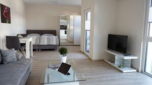 Una sala moderna con un sofá, una mesa de centro de vidrio, un televisor y un área de comedor al fondo.