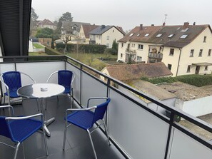 A balcony with a round table and four blue chairs, overlooking a residential area with houses and a garden. - Best Boarding 24 (Sulzbach am Main)