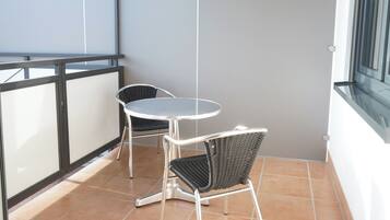 A balcony with a round table and two chairs, a tiled floor, and a window with blinds.