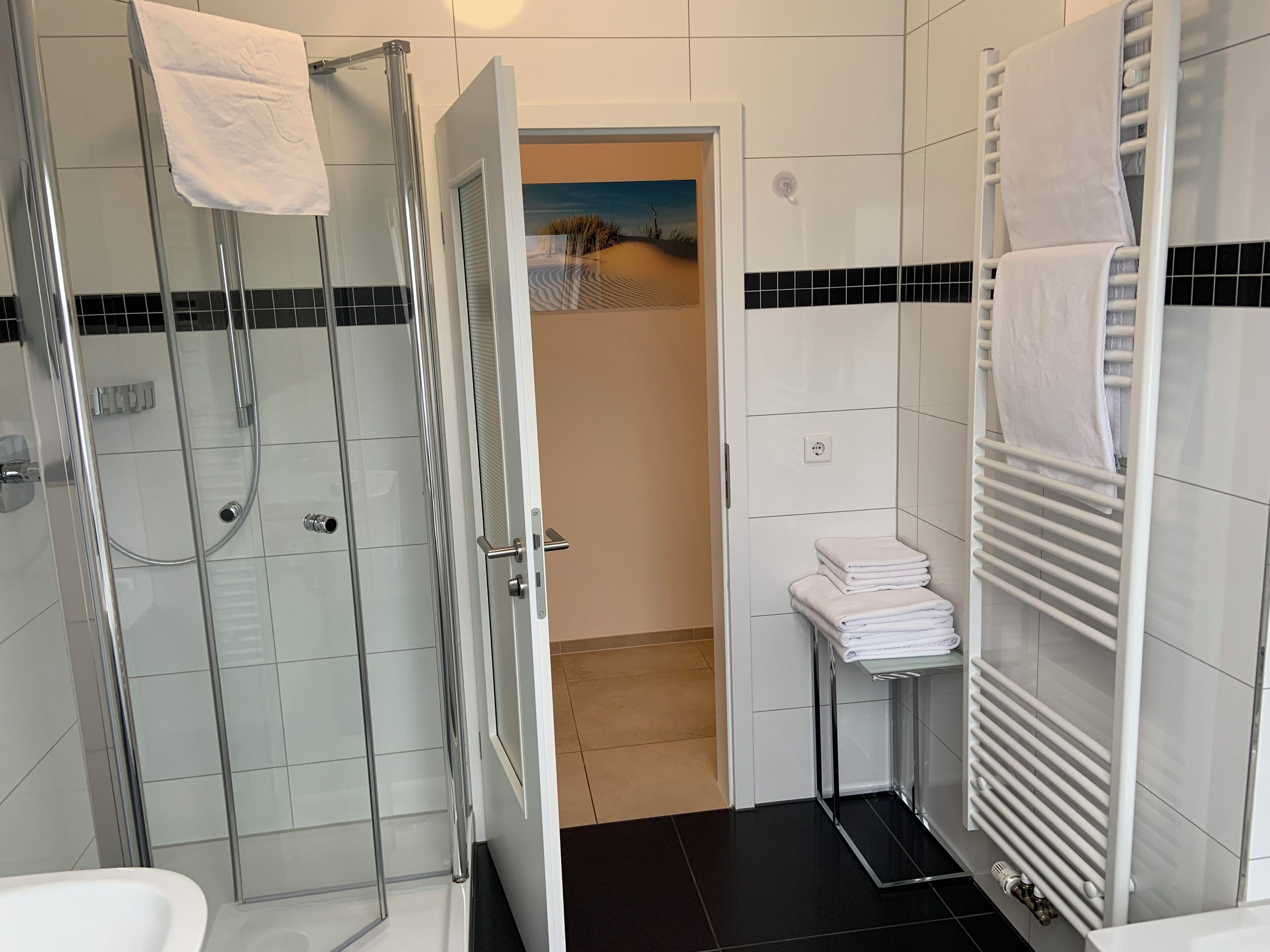 A modern bathroom with a glass shower enclosure, a white sink, and a towel rack.