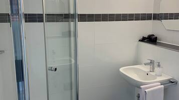 A modern bathroom with a glass shower enclosure, a white sink, and a black tiled floor.