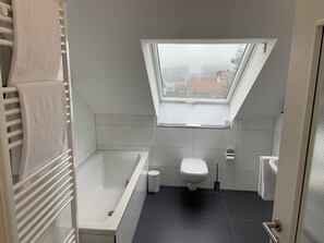 A modern bathroom with a skylight, a bathtub, a toilet, and a sink. - Best Boarding 24 (Sulzbach am Main)