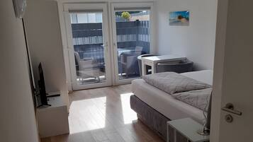 Een slaapkamer met een bed, een bureau, een stoel en een glazen schuifdeur die leidt naar een balkon.