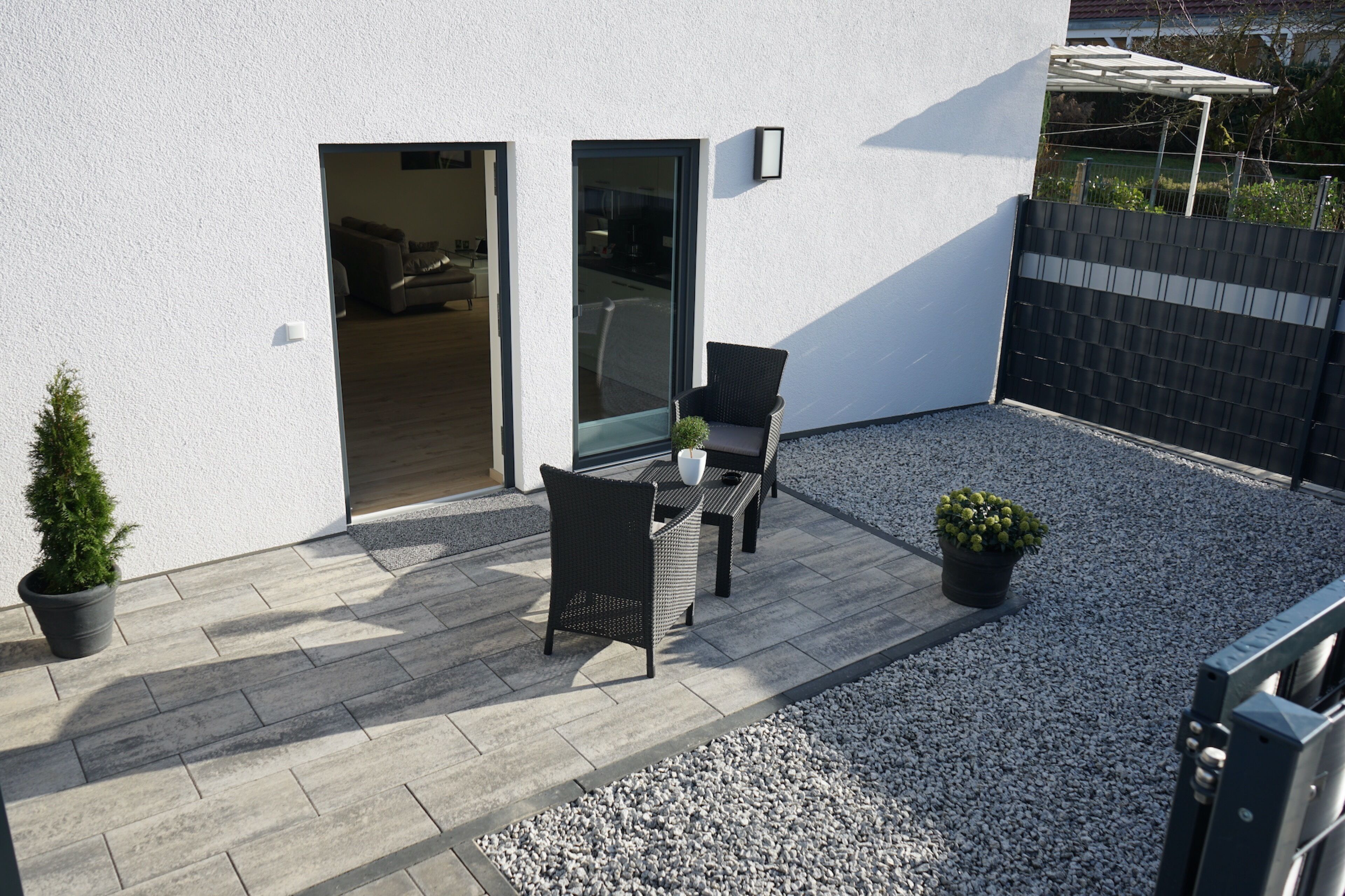 A modern outdoor patio with a seating area, a potted plant, and a gravel path.