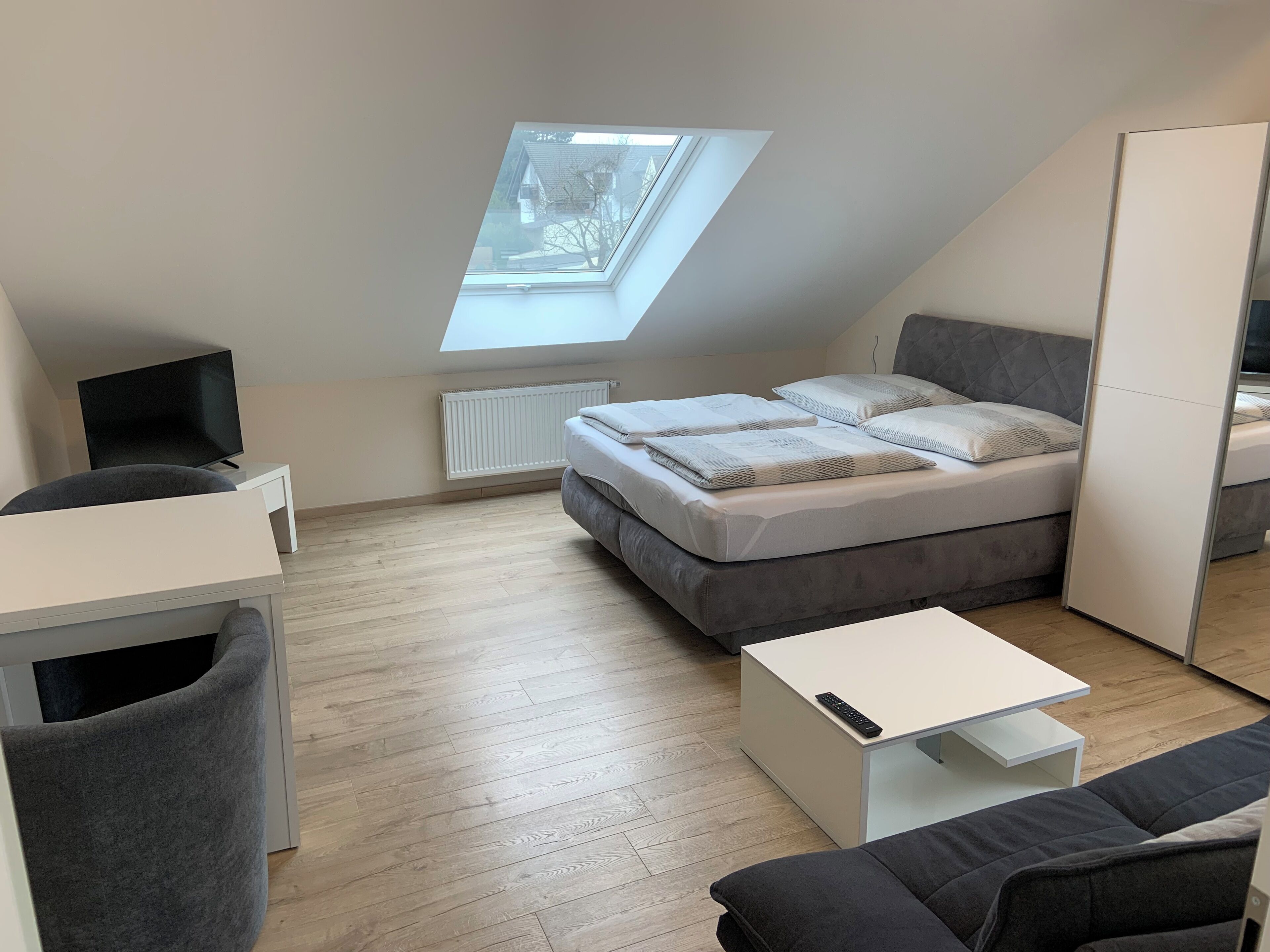 Een moderne, compacte kamer met dakraam, een bed, bureau en een slaapbank.