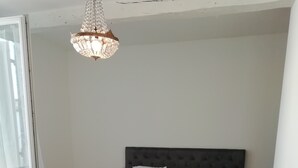 Ett sovrum med en stor säng, två sängbord, en kristallkrona och två lila fåtöljer.