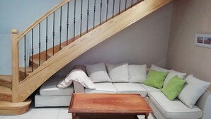 Ett vardagsrum med en trätrappa, en vit soffa, gröna kuddar och ett träbord.