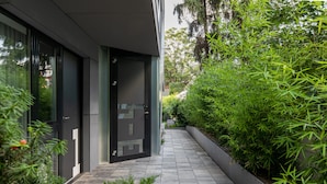 A modern building with a glass door and a pathway lined with greenery. - Blend City Center (Bucharest)
