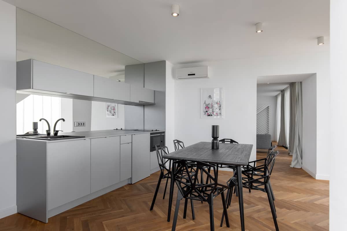A modern kitchen with grey cabinets, a central island, and a dining area with a wooden table and chairs.