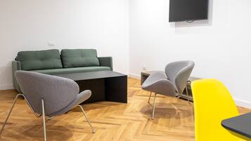 Una sala moderna con un sofá verde, dos sillones grises, una butaca amarilla, una mesa de centro negra y un televisor de pantalla plana montado en la pared.