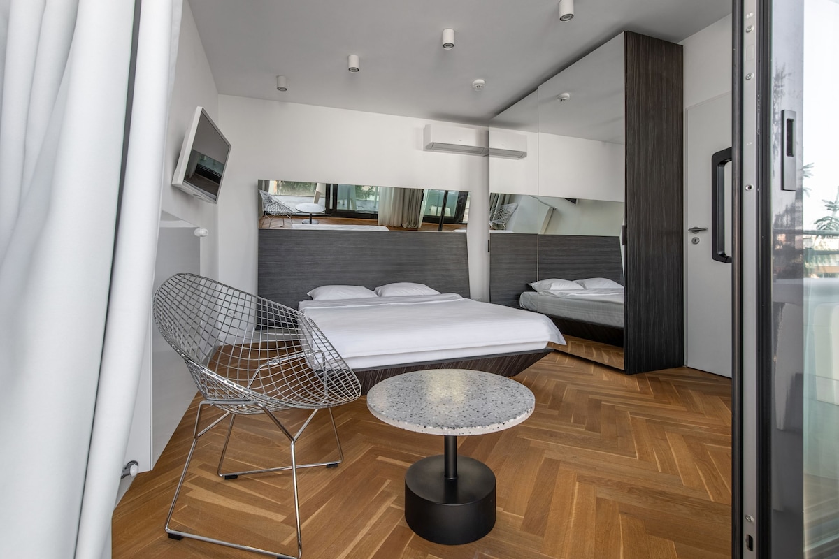 A modern hotel room with a bed, a round table, a chair, and a TV.