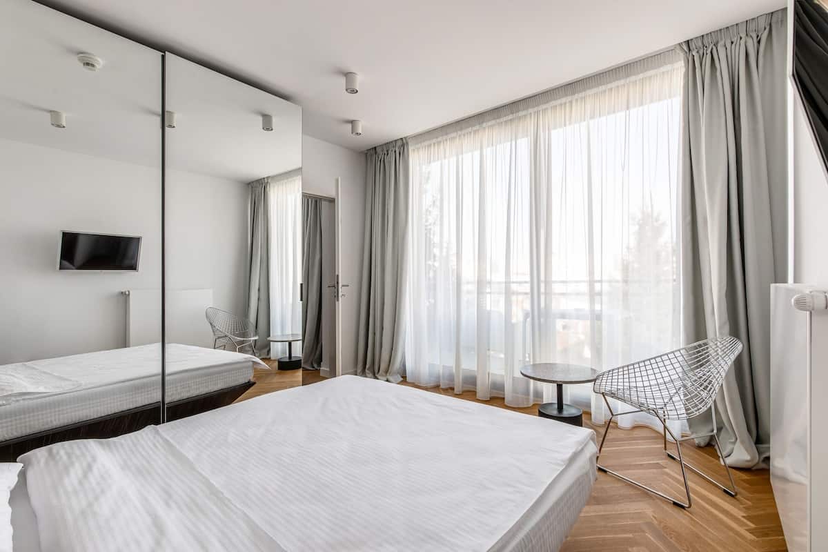 A hotel room with two beds, a TV, a chair, a small table, and large windows with curtains.