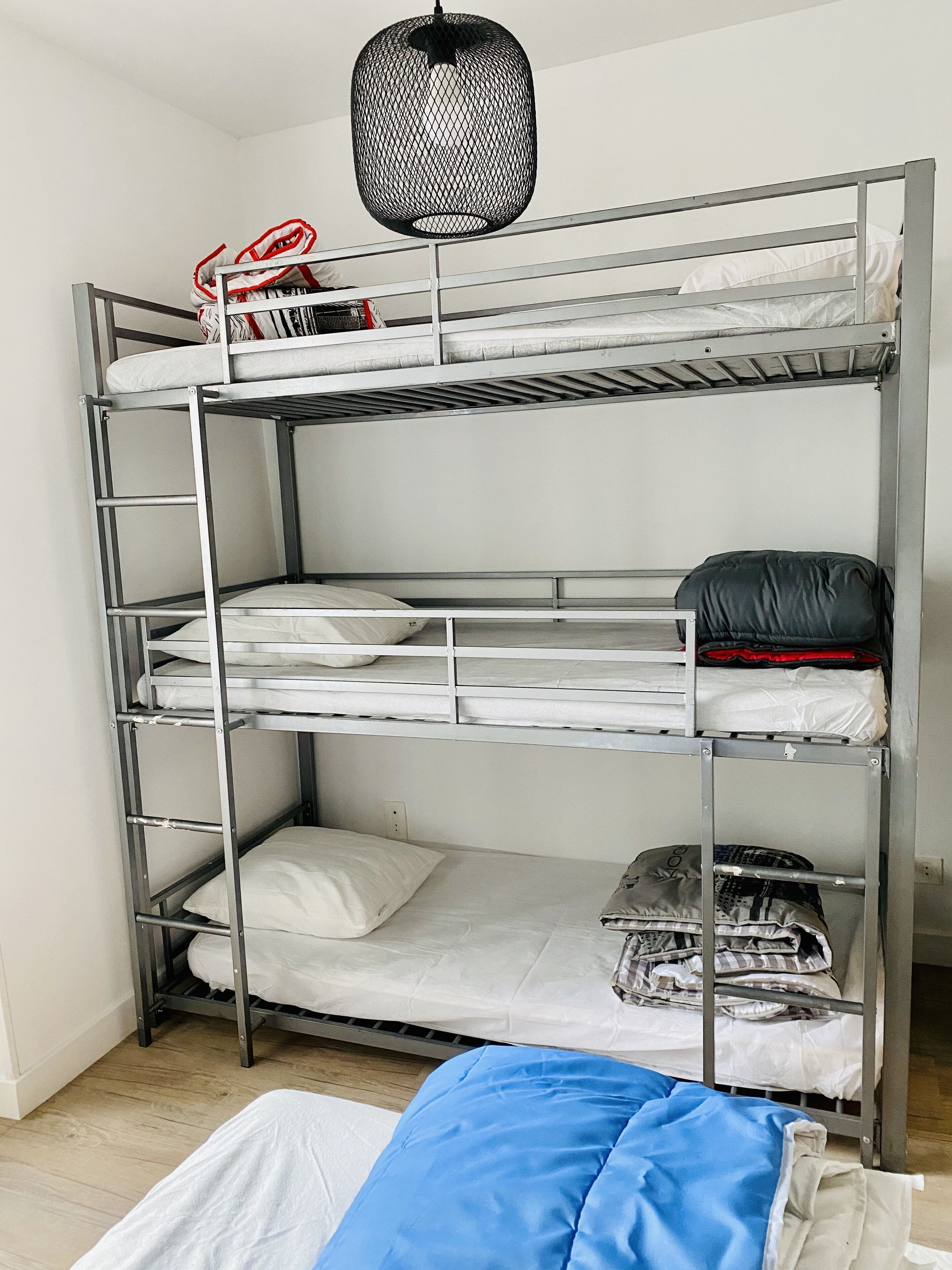 Ein Etagenbett mit Metallgestell, weißer Bettwäsche und einer Pendelleuchte.
