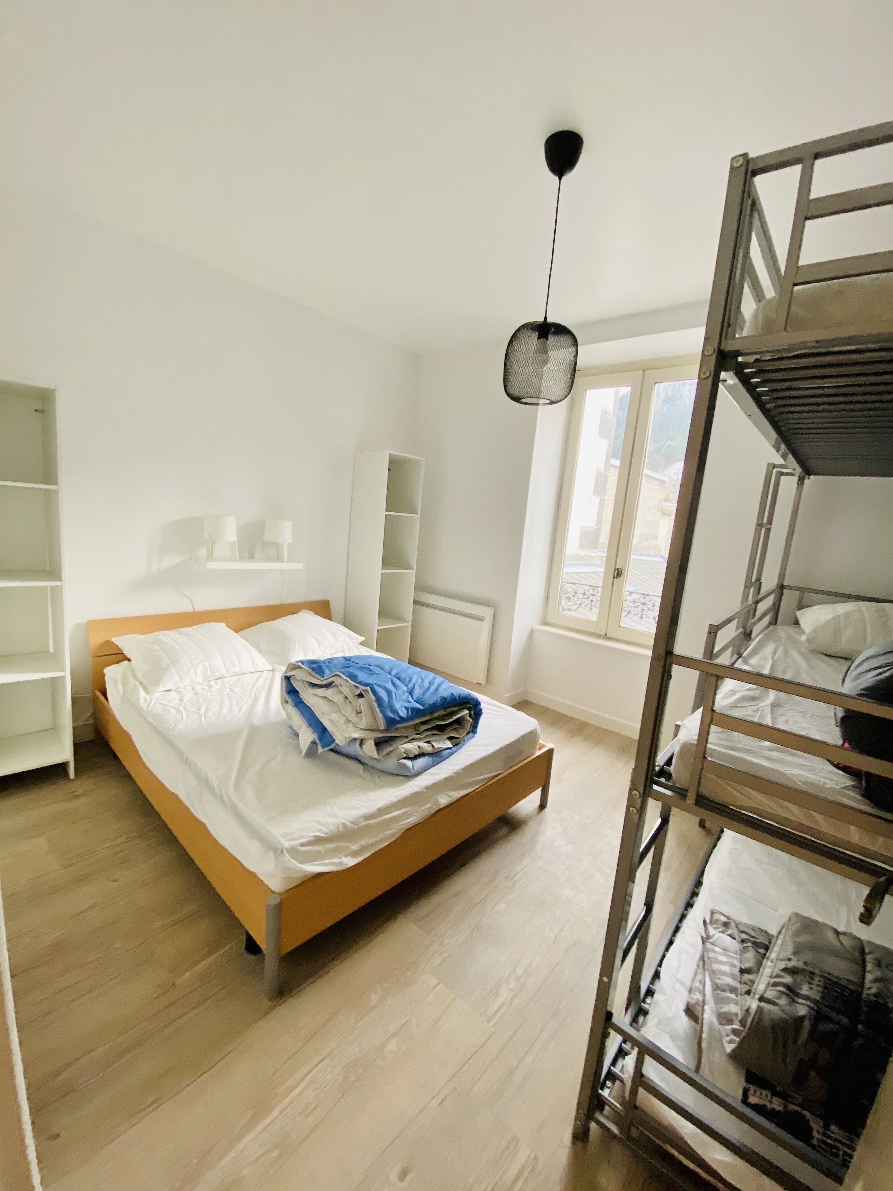A bedroom with a wooden bed, a bunk bed, white walls, and a window.