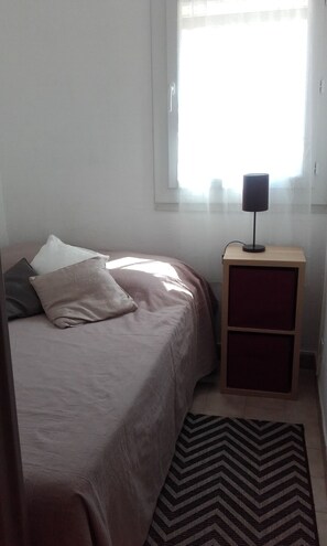 Une chambre à coucher avec un lit, une table de chevet avec une lampe, une fenêtre et un tapis.