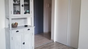 Una habitación con un armario blanco de puertas de cristal, suelo de madera y una puerta cerrada al fondo.