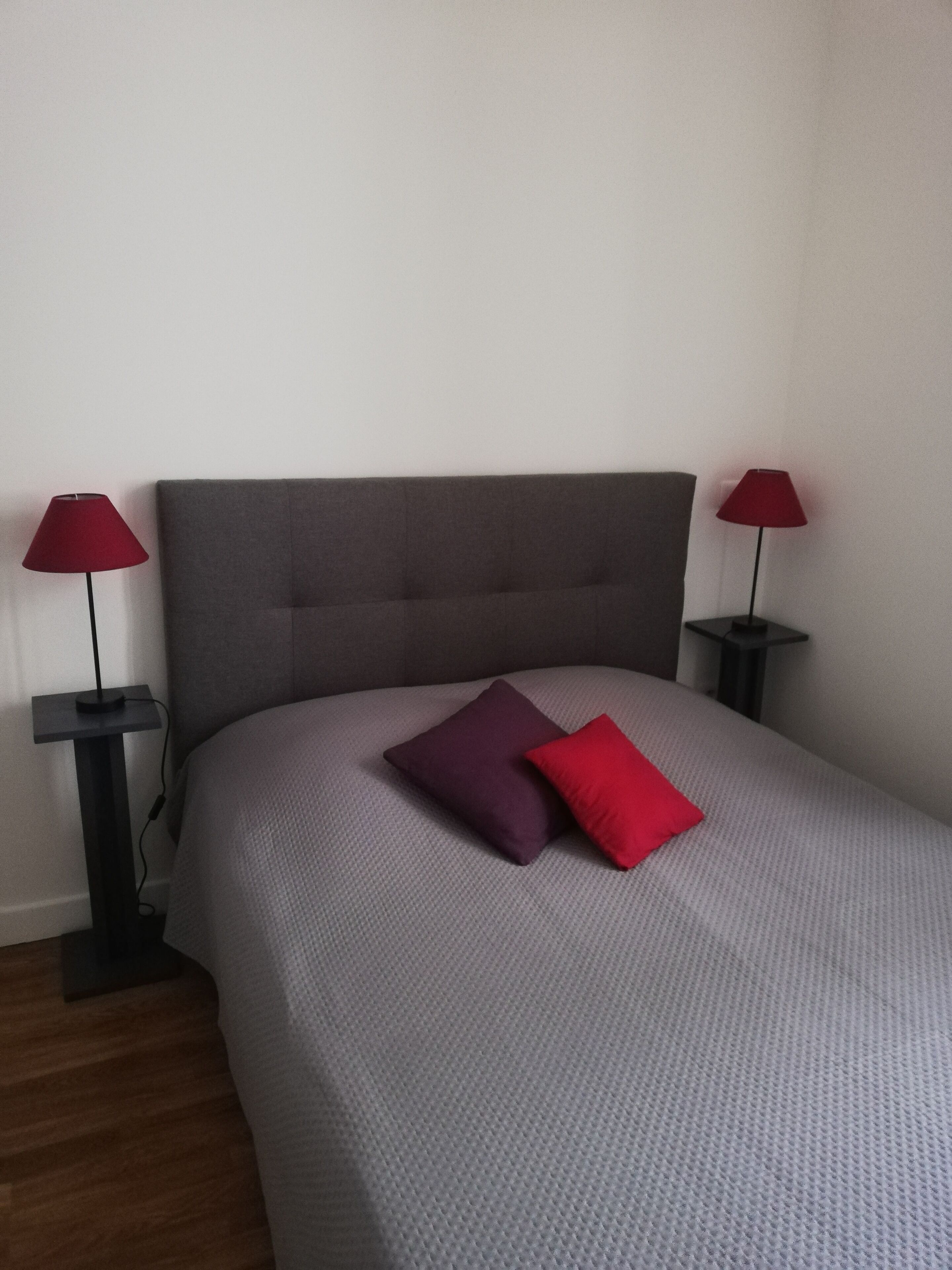 Ein Bett mit grauem Kopfteil und je einer roten Lampe auf beiden Seiten.