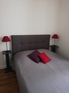 Ein Bett mit grauem Kopfteil und je einer roten Lampe auf beiden Seiten.