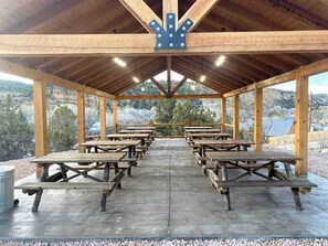 A covered picnic area with wooden benches and tables, a metal railing, and a view of the surrounding landscape. - Glamping Tent #8 with AC, Heat, and Private Bath (Orderville)