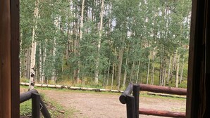 A wooden deck with a view of a forested area, a flag, and a dog. - Wolf Den Cabin is cozy and rustic that overlooks the beautiful aspens trees.   (Lake Dolores)