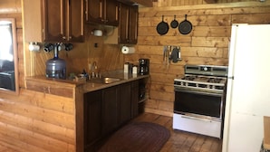 A wooden cabin kitchen with a sink, stove, and hanging pans. - Wolf Den Cabin is cozy and rustic that overlooks the beautiful aspens trees.   (Lake Dolores)