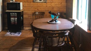 A wooden cabin interior with a round dining table, wooden chairs, a mounted telescope, a microwave on a cart, and a wolf painting on the wall. - Wolf Den Cabin is cozy and rustic that overlooks the beautiful aspens trees.   (Lake Dolores)