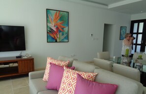 A modern living room with a flat-screen TV, a wooden entertainment unit, and a beige sofa with patterned cushions.