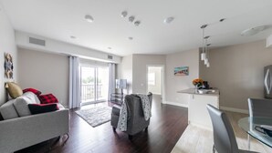 Ein modernes Wohnzimmer mit einer grauen Couch, einem gemusterten Sessel und einem Essbereich mit einem Glastisch und Stühlen.