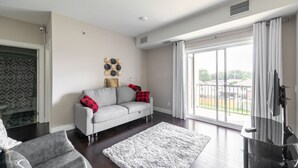 Ein modernes Wohnzimmer mit einem grauen Sofa, einem weißen Teppich und einem großen Fenster mit Vorhängen.