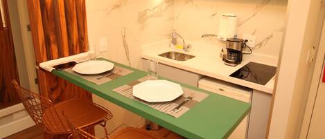 A compact kitchen with a dining area, featuring a green countertop, two pendant lights, and a microwave.