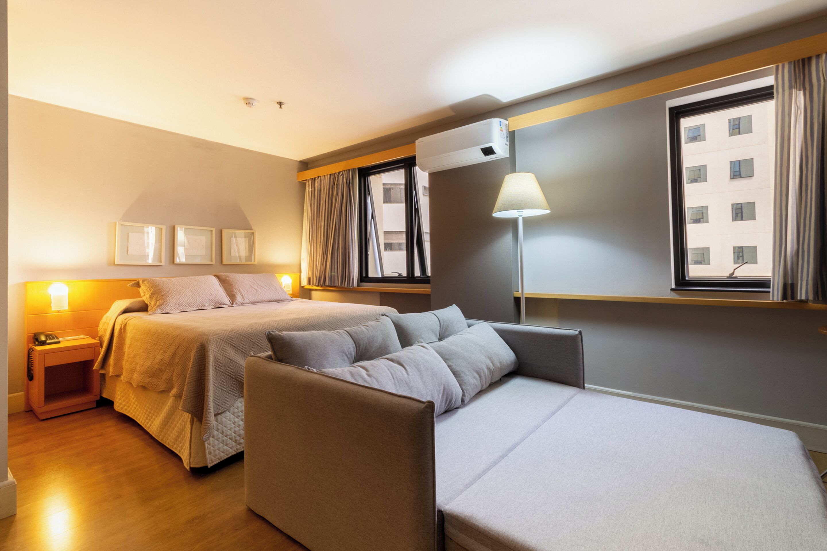 Hotellihuone, jossa on sänky, sohva, yöpöytä lampun kanssa ja ikkuna, jossa on verhot.