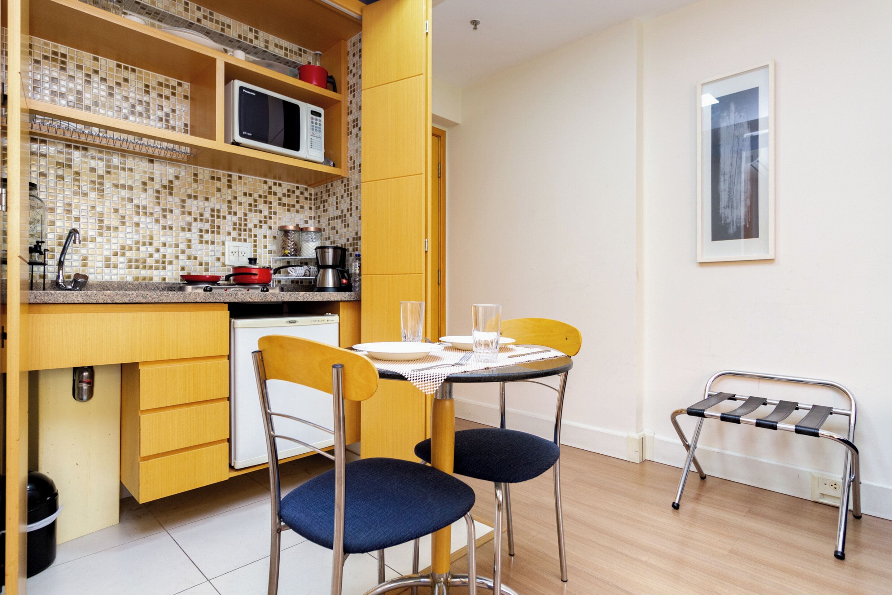 A compact kitchen with a microwave, coffee maker, and a small dining table with chairs.